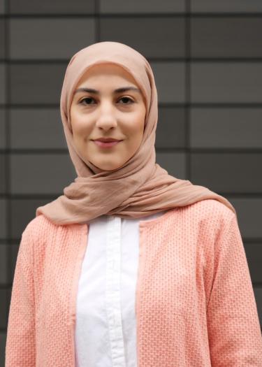 The picture shows a woman, Zeynab Tavasolyzadeh, in a white shirt and pink blouse, wearing a beige hijab. 