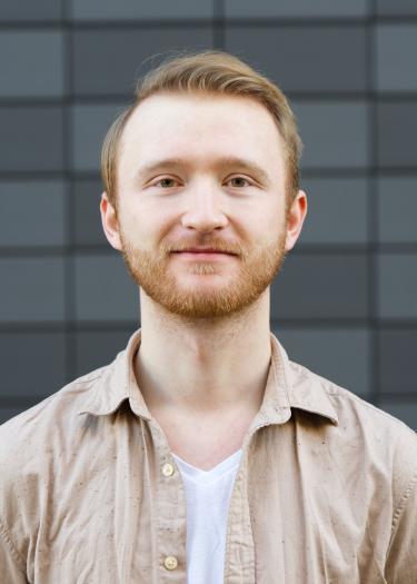 The photograph shows a man with a beard and reddish hair, Niclas Hofmann, in a beige shirt.